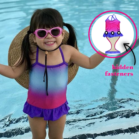 Little girl at pool wearing FASTEN swimsuit, Fuchsia Turquoise Ombre cross-back swimsuit for baby and toddler girls. Features patented design that opens at the waist, making bathroom breaks and baby diaper changes faster and easier. Sizes 6m-5. UPF 50 sun protection built right in! Cross-back swimsuit design. Ombre varies slightly in each swimsuit. Open and secured in back with hidden magnet.